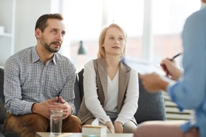 couple sitting on couch in front of psychologist and listening to her advice at couples therapy