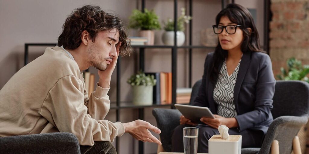 horizontal medium shot of sad young man treating depression with help of professional psychotherapist