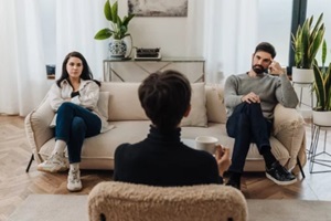 married couple sitting on opposite sides of couch during couples therapy session with psychologist