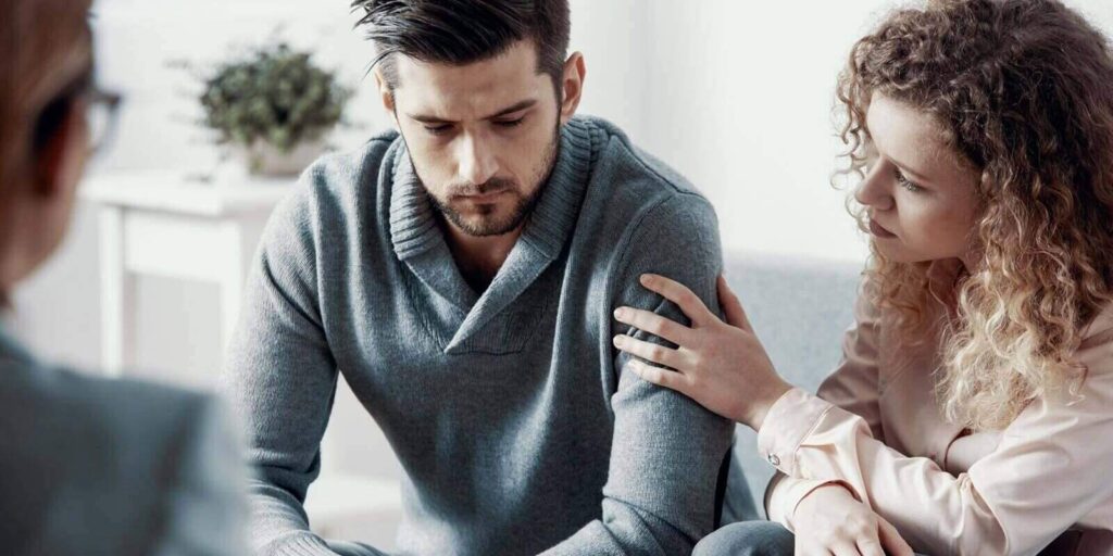 supportive beautiful wife touching husband's arm during psychotherapy session for married couples with problems