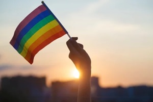 woman holding rainbow flag on sky background