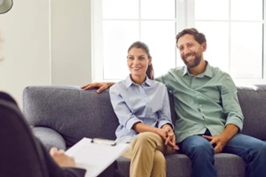 smiling couple sitting on sofa and talking with psychologist trying to find problems and solution at counselor's office