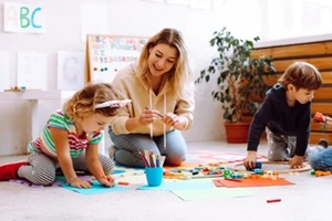 smiling female teacher play with children, make craft, colorful handmade arts in development center for special kids