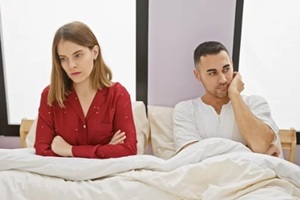 woman and man sit apart in bed, portraying tension in a modern bedroom