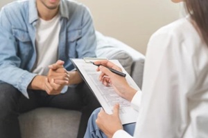 asian young man patient mental therapy explain symptom with psychologist while doctor woman taking notes at clinic