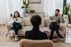 married couple sitting on opposite sides of couch during therapy session with psychologist