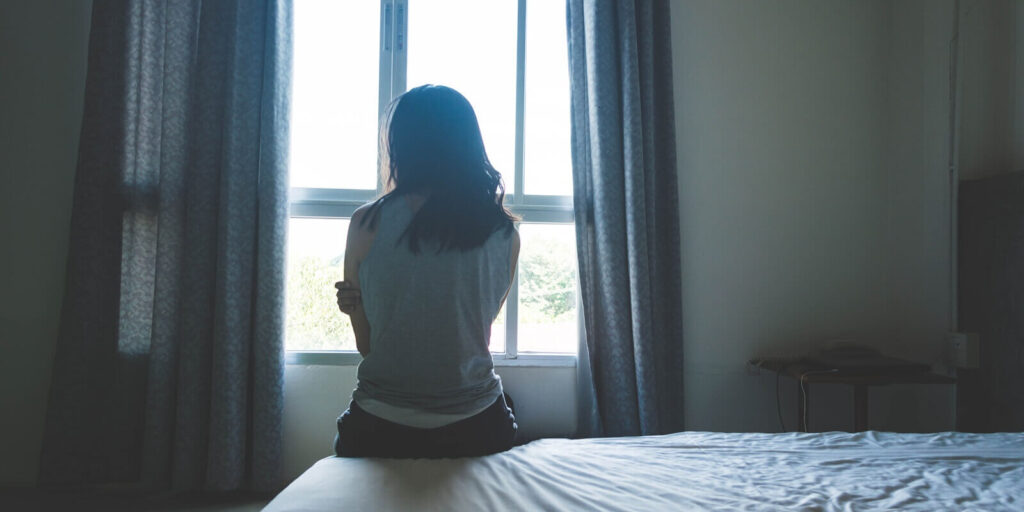 woman sitting on bed in room with light from window