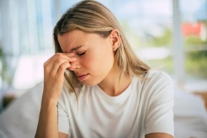 young woman sits indoors, pinching the bridge of her nose with her eyes closed during individual therapy