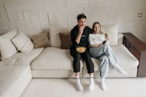 Couple Sitting on A Couch Eating Snacks and Enjoying TV