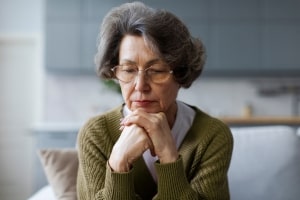 Stressed Elder Lady Sitting on Couch Looking Down
