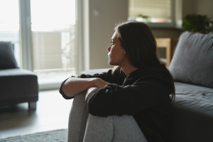 Stressed Woman Sitting at Floor and Looking Through Window at Home