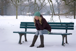Woman Sitting Alone on Snow Covered Park Bench with Winter Depression